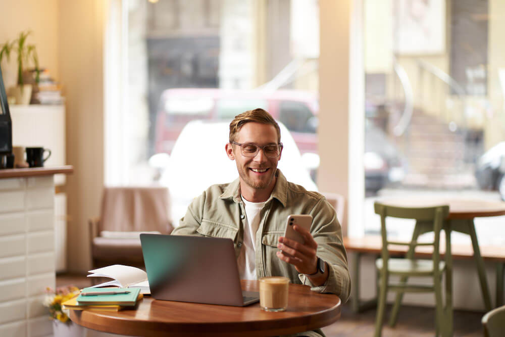 Sydney small business owner checking social media activity on a phone while working on a laptop in a cafe